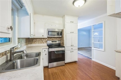 Kitchen featuring appliances with stainless steel finishes, a sink, white cabinets, decorative backsplash, and wood finished floors