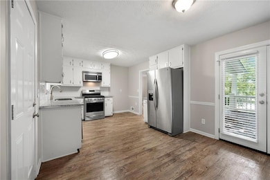 Kitchen with stainless steel appliances, a textured ceiling, wood finished floors, white cabinets, and light stone counters