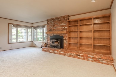 Unfurnished living room featuring ornamental molding, carpet floors, and a wood stove