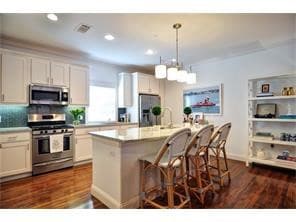 Kitchen with a breakfast bar, stainless steel appliances, a kitchen island with sink, dark wood-type flooring, and recessed lighting