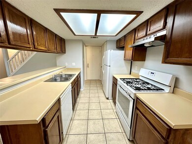 Kitchen with white appliances, light countertops, a textured ceiling, light tile patterned floors, and under cabinet range hood