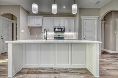 Kitchen with arched walkways, white cabinetry, stainless steel appliances, light stone countertops, and a large island with sink