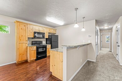 Kitchen with black appliances, a textured ceiling, a peninsula, light brown cabinetry, and light stone countertops