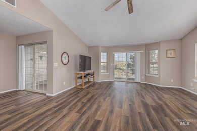 Unfurnished living room featuring vaulted ceiling, dark wood-style floors, a textured ceiling, and a ceiling fan