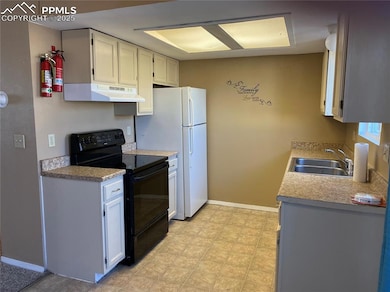 Kitchen featuring black electric range oven, a sink, under cabinet range hood, white cabinetry, and light countertops
