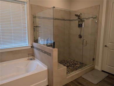 Full bathroom with a shower stall, a garden tub, and wood finished floors