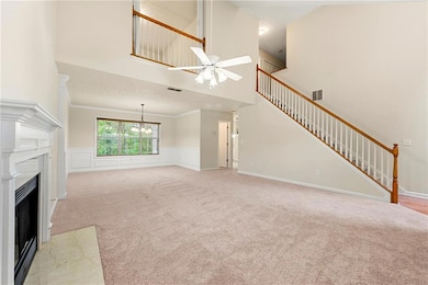 Unfurnished living room with a towering ceiling, a fireplace with flush hearth, light colored carpet, wainscoting, and a decorative wall