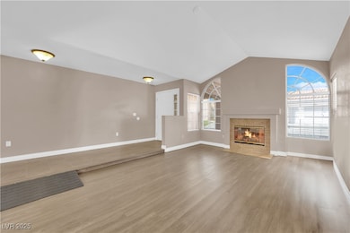 Unfurnished living room with wood finished floors, a fireplace with flush hearth, and vaulted ceiling
