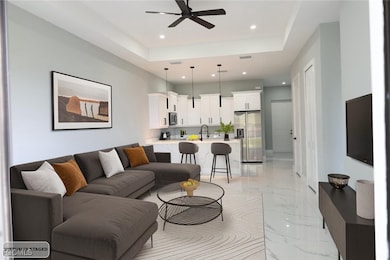 Living room featuring a tray ceiling, light marble finish flooring, recessed lighting, and ceiling fan