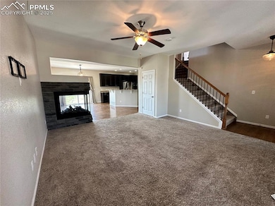 Unfurnished living room with carpet flooring, ceiling fan, stairway, and a multi sided fireplace