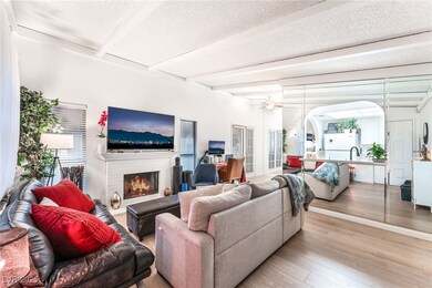 Living room featuring beamed ceiling, wood finished floors, a textured ceiling, a fireplace, and ceiling fan