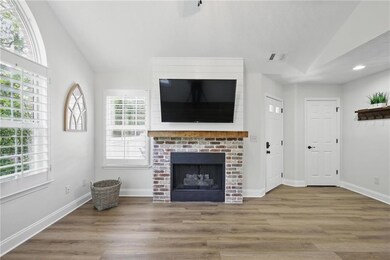 Unfurnished living room with lofted ceiling, a brick fireplace, wood finished floors, and baseboards