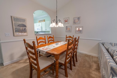 Dining room with light colored carpet, a chandelier, baseboards, vaulted ceiling, and arched walkways