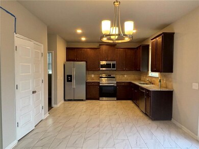 Kitchen with appliances with stainless steel finishes, a sink, a chandelier, light marble finish flooring, and baseboards
