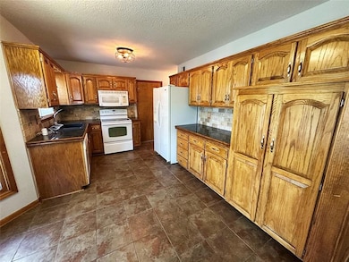Kitchen featuring brown cabinetry, white appliances, backsplash, a textured ceiling, and tile countertops