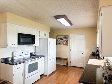 Kitchen with white range with electric stovetop, dark countertops, black microwave, a textured ceiling, and light wood-style floors