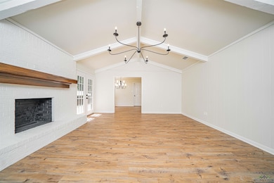 Unfurnished living room featuring a chandelier, light wood-style flooring, french doors, and a brick fireplace