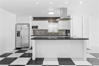 Kitchen featuring decorative backsplash, stainless steel appliances, white cabinets, sink, and island range hood