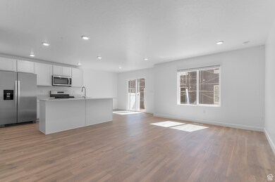 Kitchen with appliances with stainless steel finishes, open floor plan, white cabinets, a kitchen island with sink, and light countertops