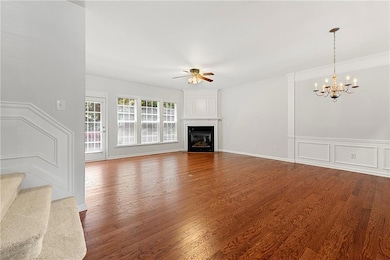 Living room featuring a ceiling fan, a chandelier, wood finished floors, a glass covered fireplace, and a wainscoted wall