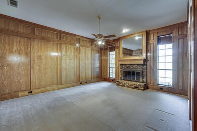 Charming living room with carpet flooring, ceiling fan, a brick fireplace, and rich wood panelling