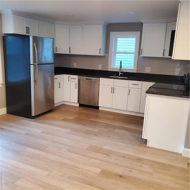 Kitchen featuring fridge, white cabinetry, stainless steel dishwasher, and dark stone counters