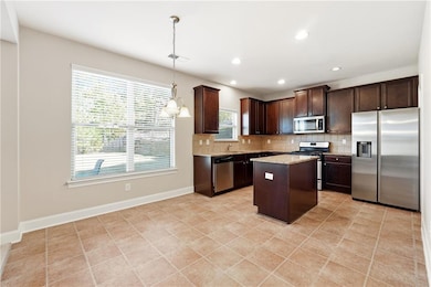 Kitchen with stainless steel appliances, tasteful backsplash, decorative light fixtures, a center island, and dark brown cabinetry