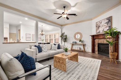 Living room featuring wood finished floors, a chandelier, crown molding, a tiled fireplace, and ceiling fan