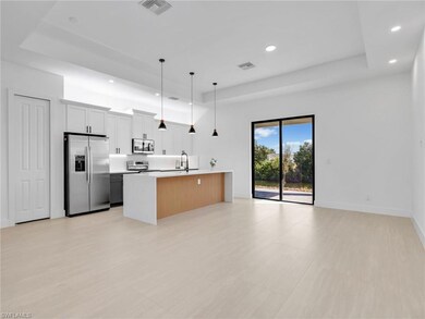 Kitchen with stainless steel appliances, hanging light fixtures, a raised ceiling, recessed lighting, and white cabinetry