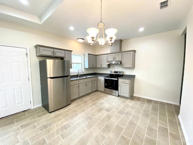 Kitchen featuring gray cabinetry, an inviting chandelier, stainless steel appliances, and light wood-type flooring