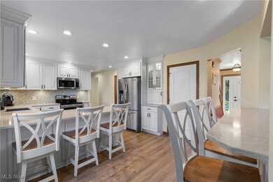 Kitchen with a kitchen bar, appliances with stainless steel finishes, glass insert cabinets, white cabinets, and light wood finished floors