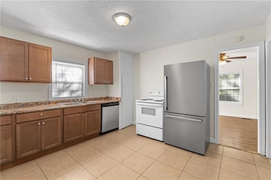 Kitchen featuring stainless steel appliances, light tile patterned flooring, a textured ceiling, brown cabinetry, and a ceiling fan