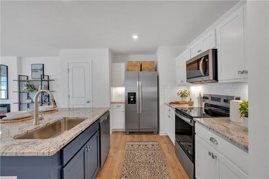 Kitchen featuring stainless steel appliances, white cabinetry, light wood finished floors, tasteful backsplash, and a center island with sink
