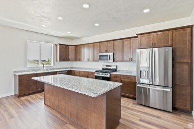 Kitchen with stainless steel appliances, light stone counters, recessed lighting, a center island, and light wood-style flooring