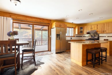 Kitchen with appliances with stainless steel finishes, tasteful backsplash, a kitchen breakfast bar, light stone counters, and light wood-style floors