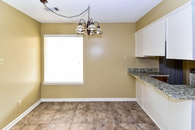 Kitchen with white cabinets, a chandelier, light stone countertops, and pendant lighting