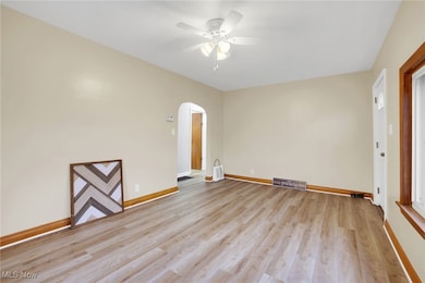 Unfurnished room featuring arched walkways, light wood-style floors, and a ceiling fan