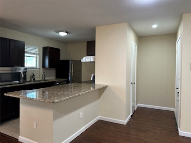 Kitchen featuring light stone counters, appliances with stainless steel finishes, a peninsula, dark wood-style floors, and dark cabinets