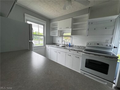 Kitchen with refrigerator, ceiling fan, electric range oven, white cabinetry, and sink