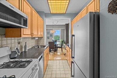 Kitchen featuring stainless steel appliances, light tile patterned floors, dark countertops, tasteful backsplash, and a chandelier