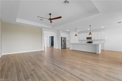 Unfurnished living room with a raised ceiling, arched walkways, a ceiling fan, light wood-style flooring, and recessed lighting