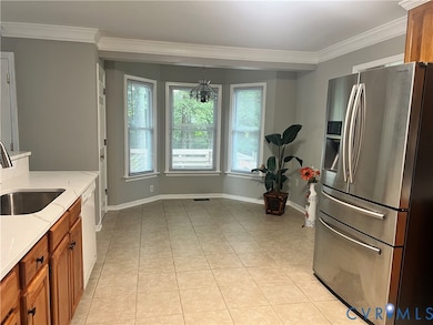 Kitchen with stainless steel fridge, brown cabinets, crown molding, light stone counters, and light tile patterned floors
