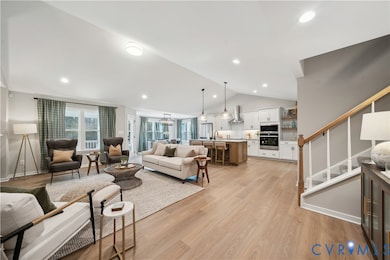 Living area featuring lofted ceiling, light wood-style flooring, a chandelier, recessed lighting, and stairway