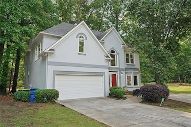 Traditional-style home with stucco siding, an attached garage, driveway, and view of wooded area