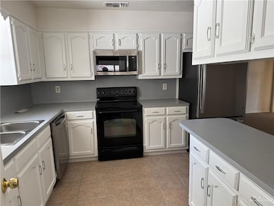 Kitchen with appliances with stainless steel finishes, white cabinets, light tile patterned flooring, and light countertops