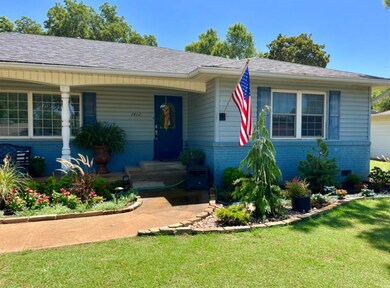 View of front of property featuring brick siding, a front lawn, roof with shingles, and a porch