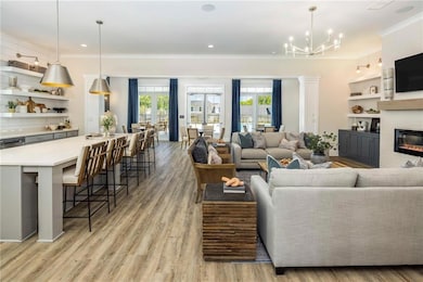 Living area with ornamental molding, a chandelier, a glass covered fireplace, light wood finished floors, and built in shelves