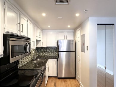 Kitchen with appliances with stainless steel finishes, dark stone countertops, decorative backsplash, light wood-type flooring, and white cabinetry