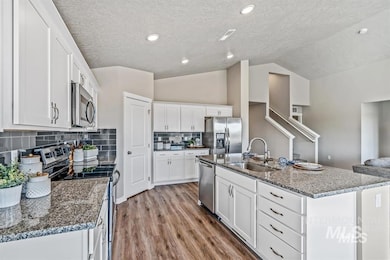 Kitchen featuring stainless steel appliances, white cabinetry, vaulted ceiling, a textured ceiling, and light wood finished floors
