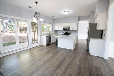 Kitchen featuring stainless steel appliances, light countertops, a kitchen island, white cabinets, and dark wood-type flooring